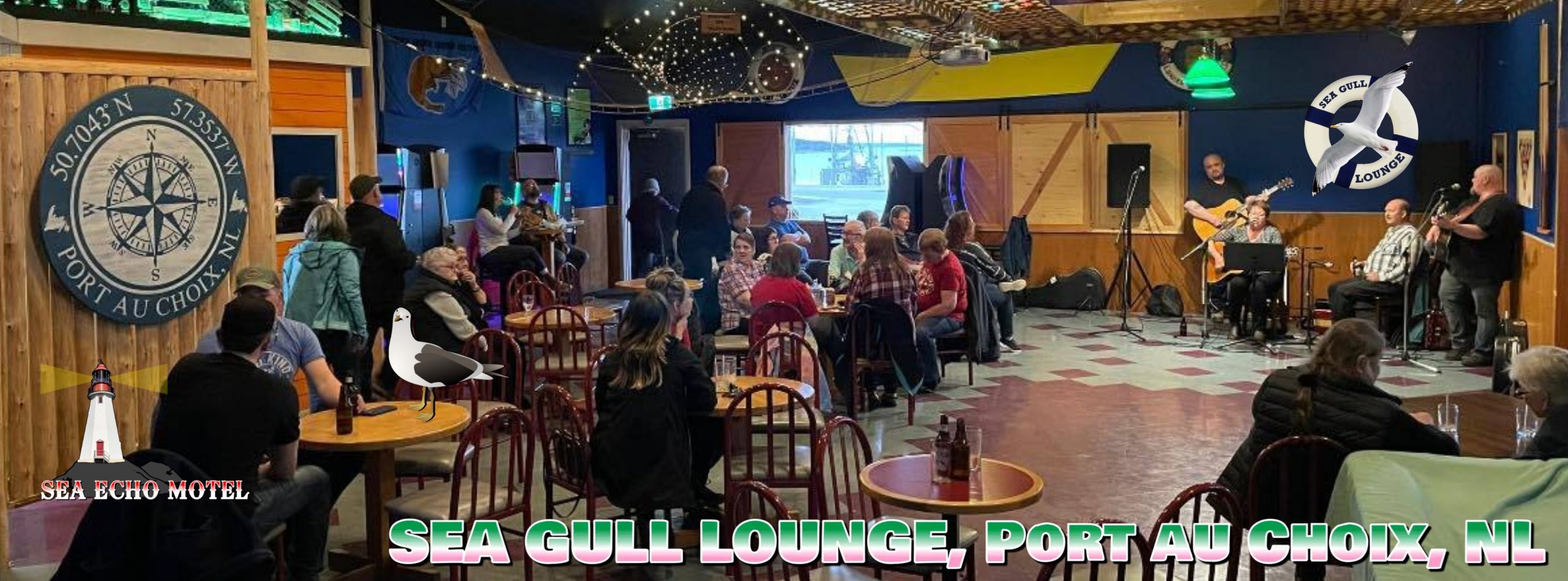 This image shows the interior of the Sea Gull Lounge in Port au Choix, NL, a cozy, nautical-themed venue attached to the Sea Echo Motel. The lounge features wood-paneling, a compass mural, string lights overhead, and a corner stage with microphones and musicians performing for a seated, engaged crowd. The casual setup with mixed seating, arcade machines in the back, and a clearly defined stage area makes it a perfect space for intimate live performances like stand-up comedy or acoustic music. The relaxed community vibe and charming decor capture the essence of a great small-town venue.